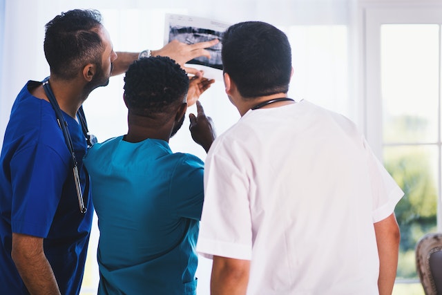 Drei männliche Ärzte schauen sich ein Röntgenbild an.